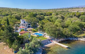 A villa with a swimming pool, surrounded by lush greenery and a mountainous backdrop.
