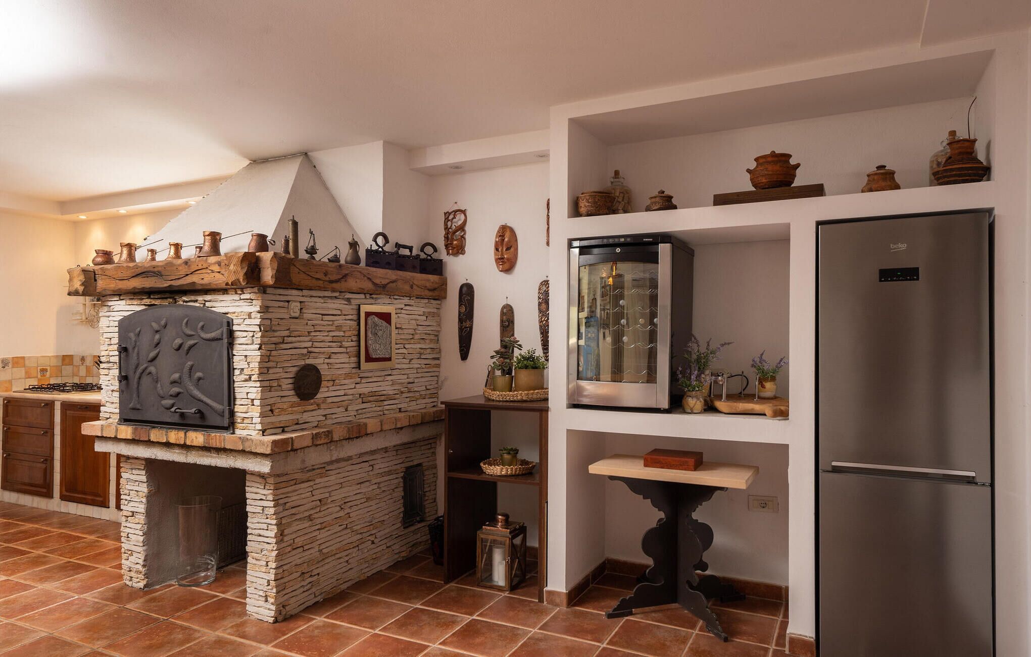 Une cuisine équipée d’un four en pierre, d’un réfrigérateur et de divers objets décoratifs disposés sur des étagères.