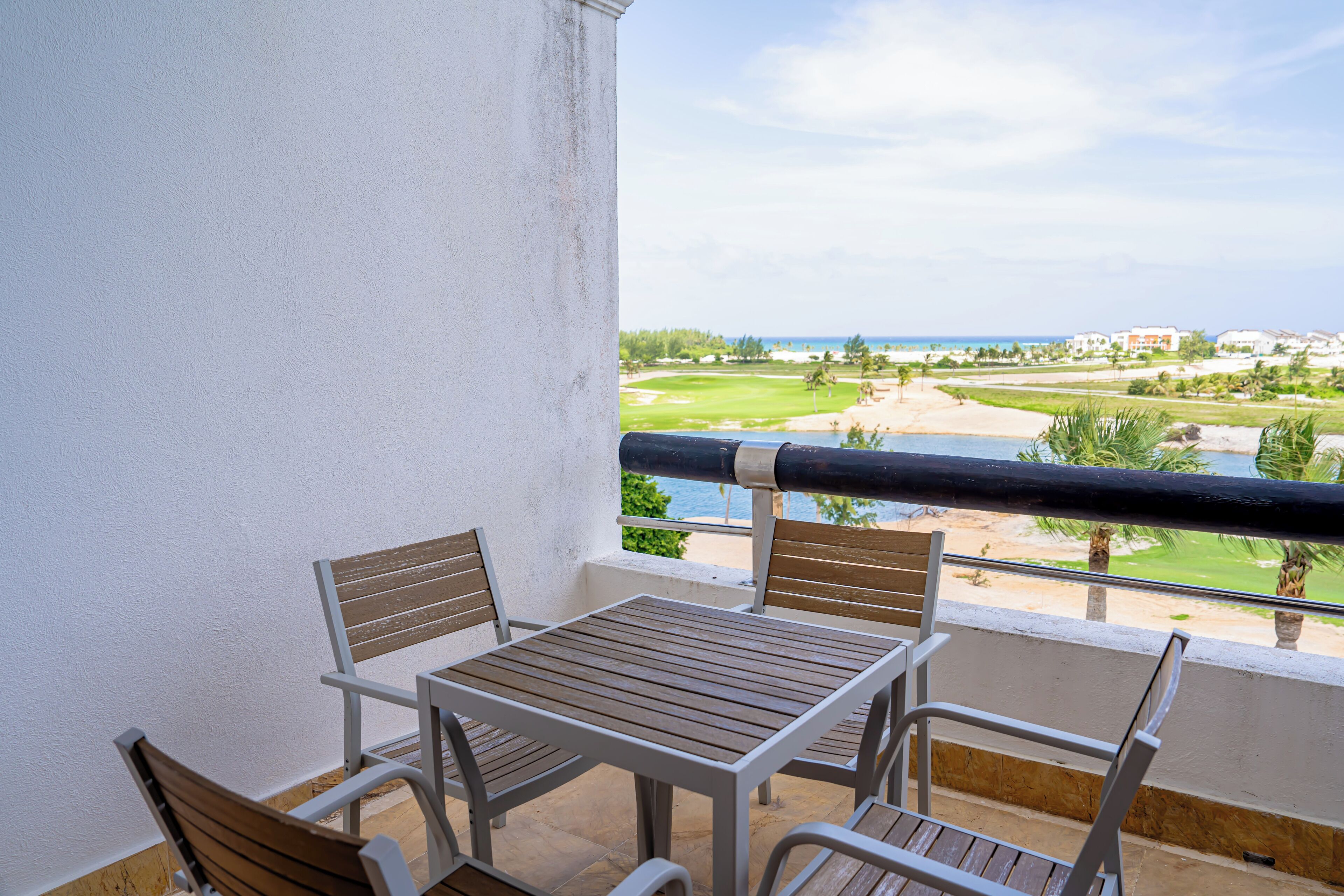 A balcony with a table and chairs, overlooking a golf course and beach.