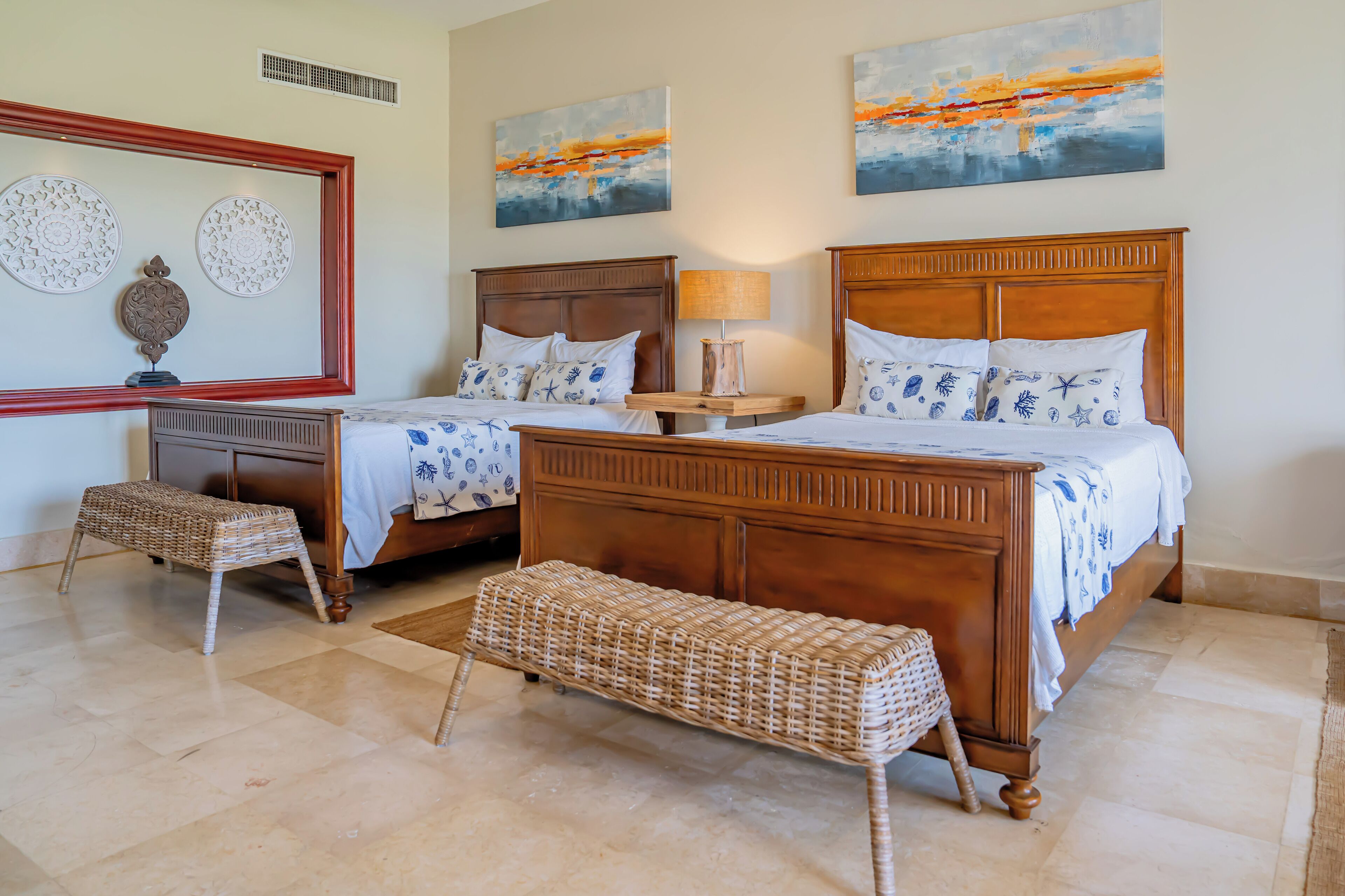 A bedroom with two wooden beds, a wicker bench, a nightstand, and wall art.