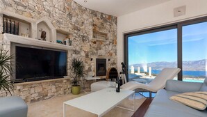 Una sala de estar moderna con chimenea de piedra, televisor de pantalla plana y un ventanal con vistas panorámicas.