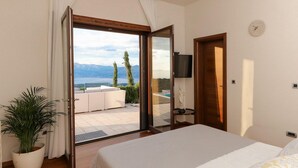 Un dormitorio con cama, televisión, reloj y vistas a una piscina y montañas.