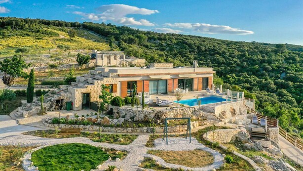 Una villa moderna con piscina, arquitectura de piedra y un jardín exuberante.