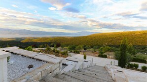 Una escalera de piedra que lleva a una terraza con vistas a un paisaje montañoso, donde se divisan colinas lejanas y una masa de agua.