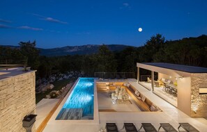 Un área de piscina moderna al aire libre con una cascada, rodeada de muros de piedra y asientos de madera.