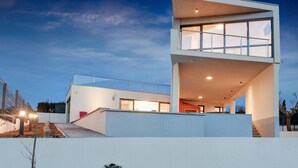 Ein modernes, zweistöckiges Haus mit flachem Dach, großen Fenstern und einer Treppe, die zum oberen Stockwerk führt.