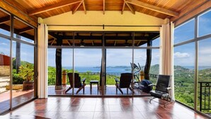 Un balcon spacieux doté d’un plafond en bois, de grandes portes vitrées et d’une vue sur la mer.