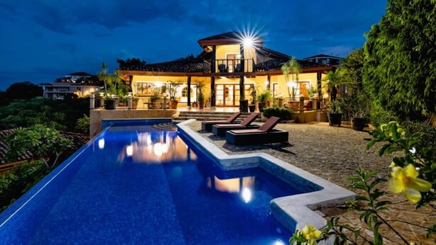 Une grande maison avec une piscine, un espace extérieur aménagé pour s’asseoir et une terrasse bien éclairée.