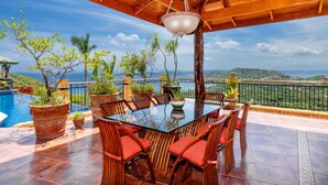 Un espace extérieur abrité, aménagé pour prendre les repas, avec une table et des chaises, entouré de plantes en pot et offrant une vue panoramique.