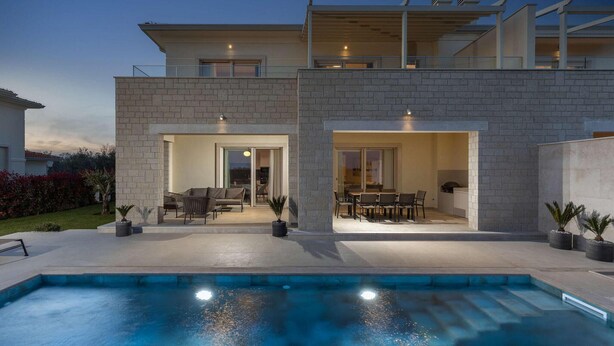 Een modern huis met twee verdiepingen, een zwembad, buitenmeubilair en een overdekt terras.
