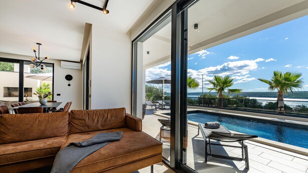 Una sala de estar moderna con un ventanal grande que da a una piscina y vistas panorámicas.