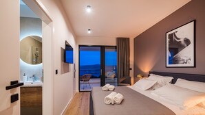 Una habitación de hotel moderna con una cama grande, televisión de pantalla plana, baño con espejo y balcón con vistas.