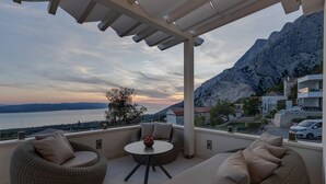 Una terraza con mobiliario de mimbre, una mesa redonda y vistas a un lago y montañas.