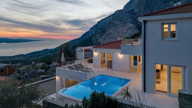 Una villa moderna con piscina, ventanas amplias y vistas al mar y a las montañas.