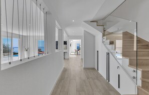 A modern interior with a staircase, a dining area, and a view of the sea.