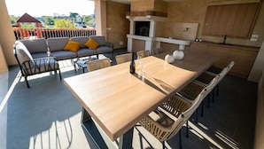 Una cocina moderna al aire libre con comedor, que incluye una mesa de madera y sillas de mimbre.