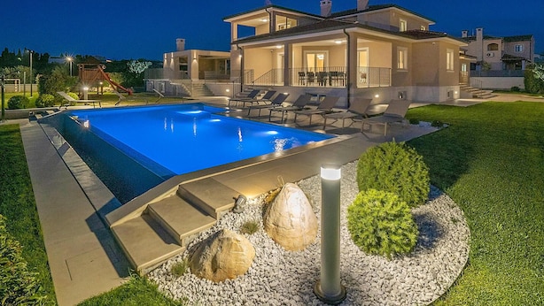 Una casa moderna con piscina, zona de estar exterior y un patio bien iluminado.
