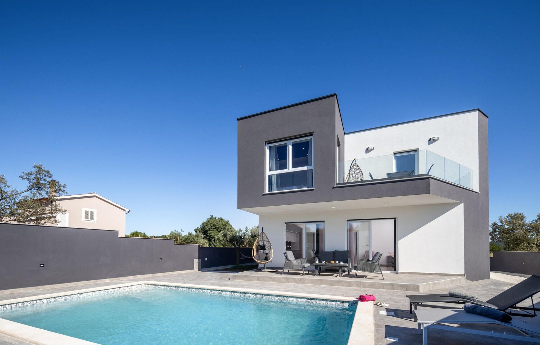 Une maison moderne à deux étages dotée d’une piscine, d’un espace salon extérieur et d’un balcon.