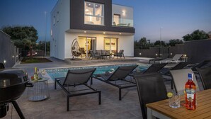 Une maison moderne dotée d’une piscine, d’un espace salon extérieur et d’un coin barbecue.