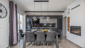 Une cuisine moderne avec des meubles de couleur sombre, un four encastré et un coin repas comprenant une grande table et des chaises.