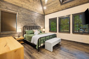 Ein Schlafzimmer mit Holzboden, einem Bett mit grüner Bettwäsche, einer Bank und einem Fernseher an der Wand.