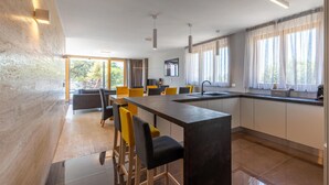 Una cocina moderna con una isla central, taburetes de bar y una zona de comedor con sillas amarillas.
