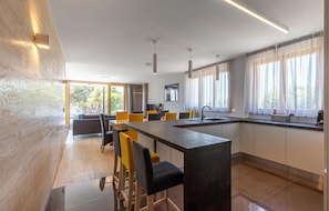 Una cocina moderna con una isla central, taburetes de bar y una zona de comedor con sillas amarillas.