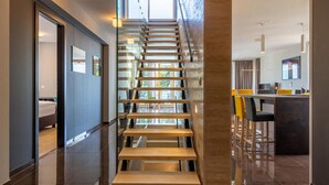 Un interior moderno con una escalera de cristal, una zona de comedor con sillas amarillas y una cocina con barra.
