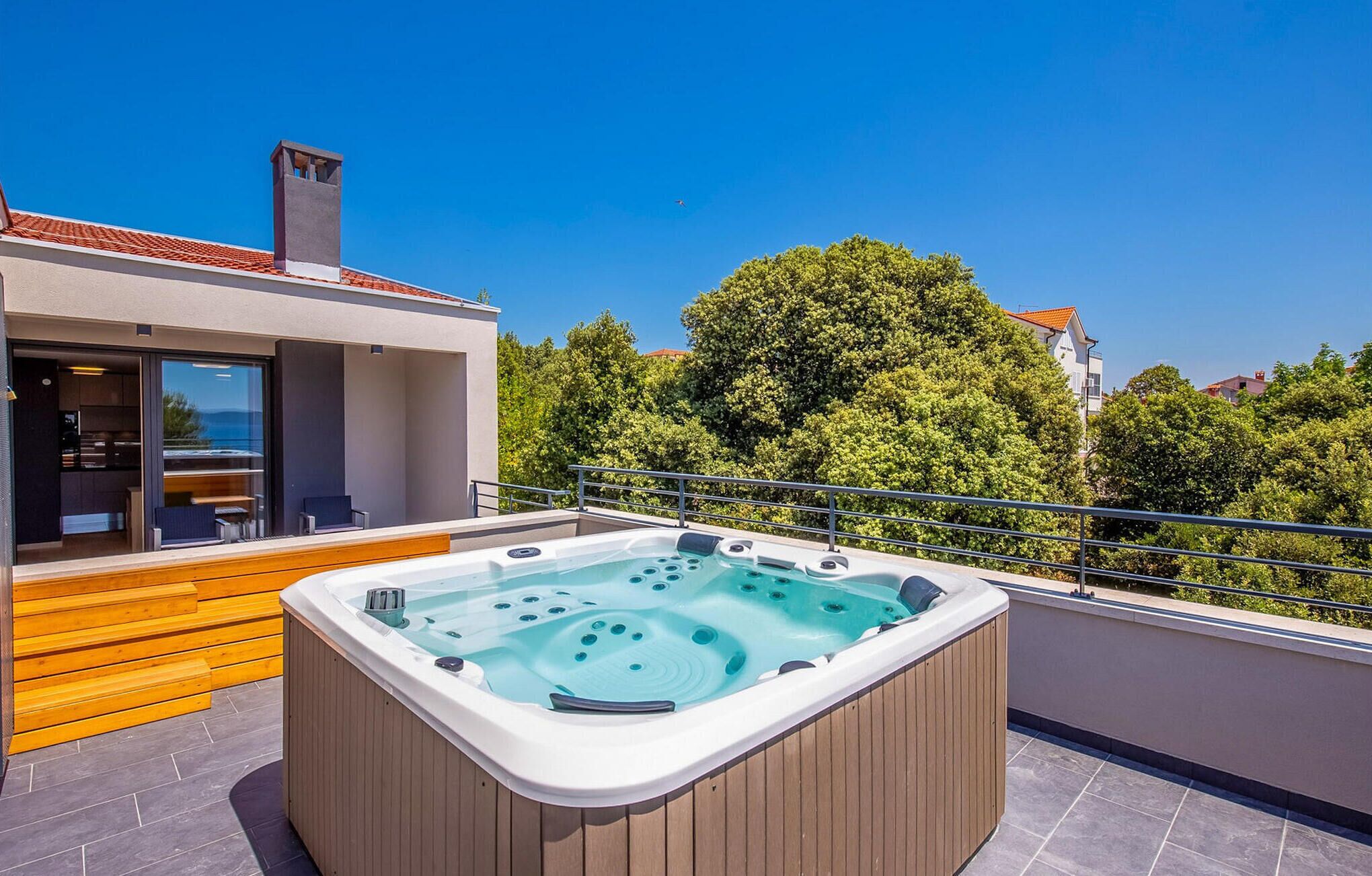 A modern outdoor hot tub on a balcony with a clear view of the surrounding trees and buildings.