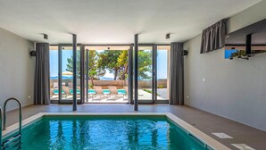 Una piscina con agua azul cristalina, rodeada por un cerramiento de vidrio que ofrece vistas a una zona de piscina y árboles.