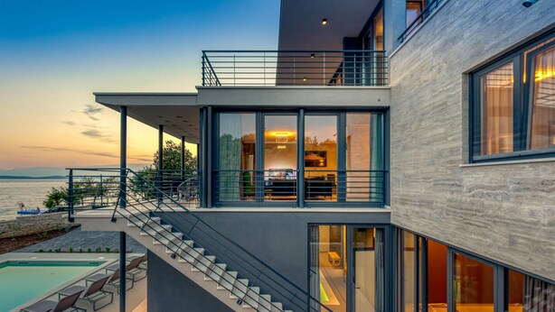 Una casa moderna con piscina, mobiliario exterior y una escalera que conduce a un balcón.