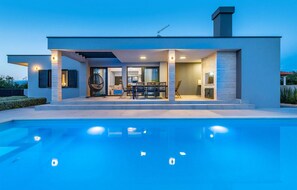 Een modern huis met een zwembad, een terras met tuinmeubels en een groot raam met uitzicht op het zwembad.
