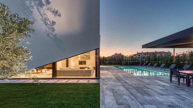 Una casa moderna con un amplio ventanal de vidrio, una piscina y un césped cuidado.