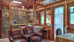 A cozy cabin interior with a wooden interior, a kitchen area with a refrigerator and shelves, a dining table with chairs, and a large window. - Nice home in Wilcze with sauna (Wilcze)