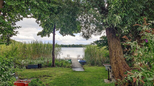 A wooden dock leading to a calm lake, surrounded by lush greenery and trees. - Nice home in Wilcze with sauna (Wilcze)