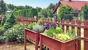 A garden with raised beds, a wooden fence, and a building with a red roof in the background. - Nice home in Wilcze with sauna (Wilcze)