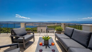Un balcon avec deux canapés gris, une petite table sur laquelle reposent deux verres contenant une boisson rouge, et une plante en pot.