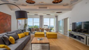 Un salon moderne avec un canapé gris, des coussins jaunes, une table basse en bois et un téléviseur posé sur un meuble.