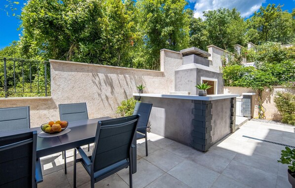 Une terrasse extérieure avec une table et des chaises, un petit coin cuisine et un mur en pierre.
