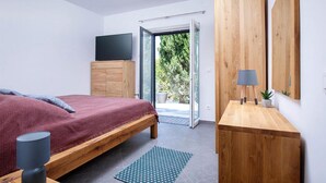 A modern bedroom with a wooden bed, a TV on a wooden cabinet, and a view of the outdoors through a glass door. - Nice home in Splitska (Splitska)