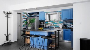 A modern kitchen with blue cabinets, a stainless steel island with stools, and a decorative plant. - Nice home in Splitska (Splitska)