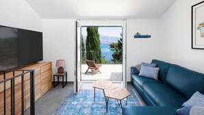 A modern living room with a large TV, a blue sofa, a wooden cabinet, and a view of a balcony with a chair and a table. - Nice home in Splitska (Splitska)