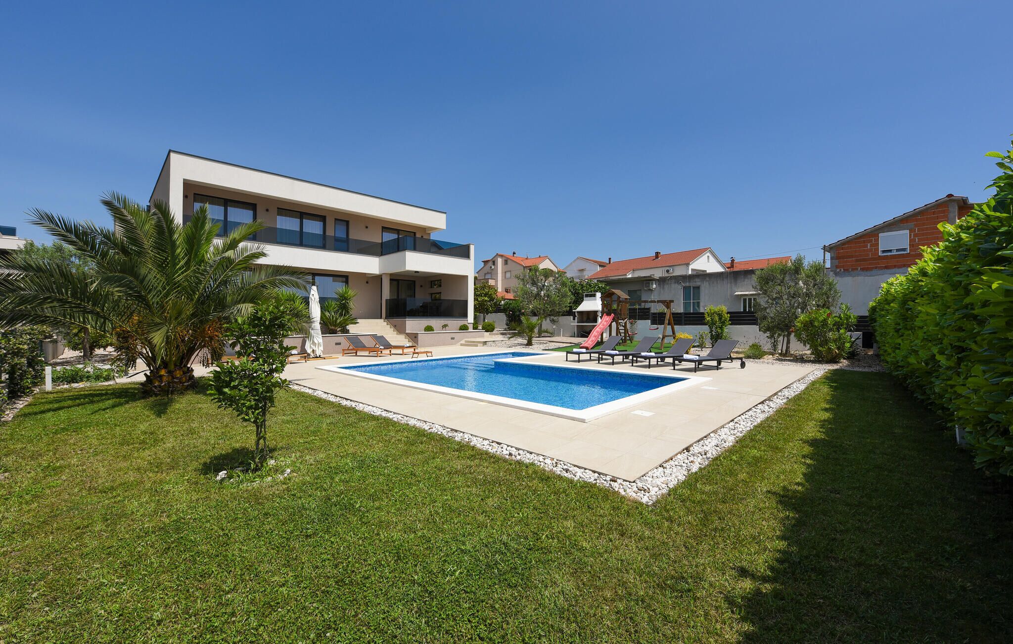 Uma casa moderna com dois andares, piscina, escorrega e um pequeno jardim.