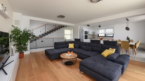 En moderne stue med en modulsofa, et rundt sofabord og en trappe, der fører til en etage ovenpå.