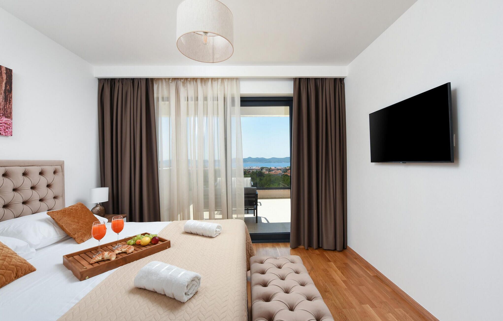 A hotel room with a bed, a TV, a balcony with curtains, and a breakfast tray on the bed.