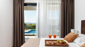 Et hotelværelse med en seng, et bakke med croissanter, frugt og juice, samt udsigt til en pool og landskab.