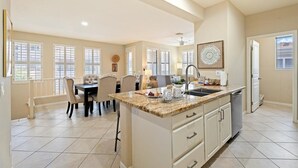 A spacious kitchen with a central island, a dining area with a table and chairs, and a view of the outside through large windows. - Peaceful Kierland 2BR Condo | Pool, Spa | Free Parking | Golf Access | Gym Walk to Shops & Dining (Scottsdale)