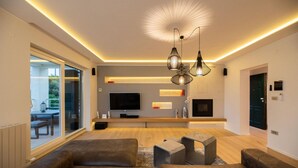 Un salon moderne avec un téléviseur, un canapé et des luminaires suspendus.