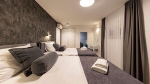Una habitación de hotel moderna con una cama grande, una cama más pequeña, un escritorio con espejo y un baño visible a través de una puerta abierta.