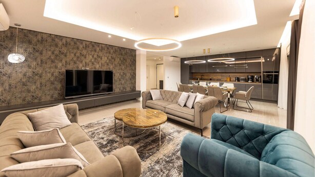 Una sala de estar moderna con un televisor grande, un sofá, una mesa de centro y un comedor con una cocina al fondo.